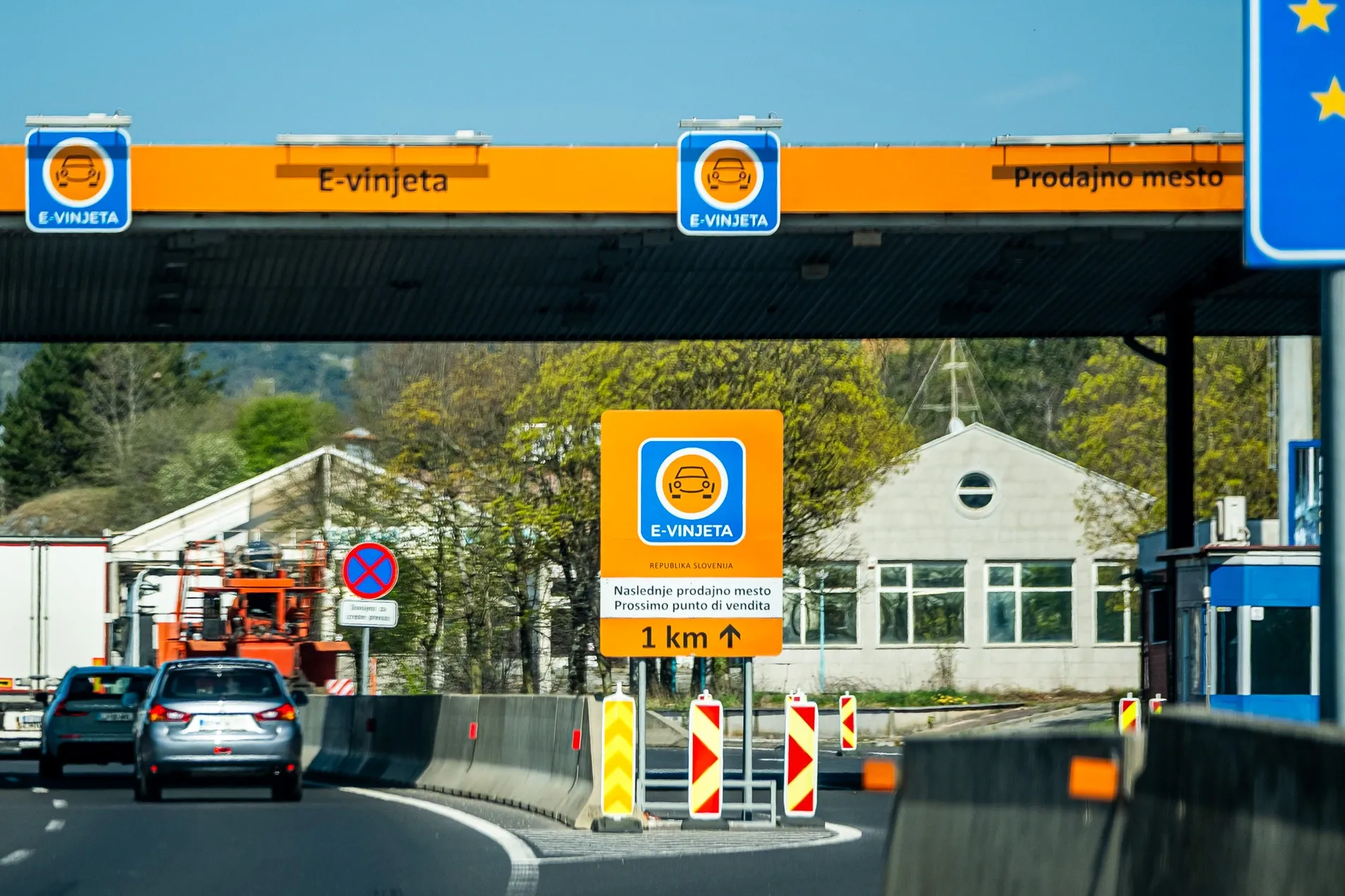 Slovenia E-Vinjeta orange gantry and prodajno mesto sales point sign at border crossing with next vignette sales point in 1km ahead sign in Slovenian and Italian, April 2026