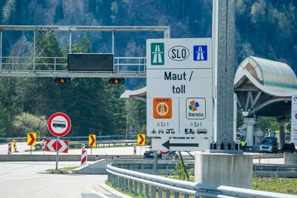 Slovenia SLO Maut toll sign at Karavanke border showing Vinjeta e-vignette for vehicles under 3.5t and DarsGo system for vehicles over 3.5t with Karavanke tunnel architecture visible, April 2026